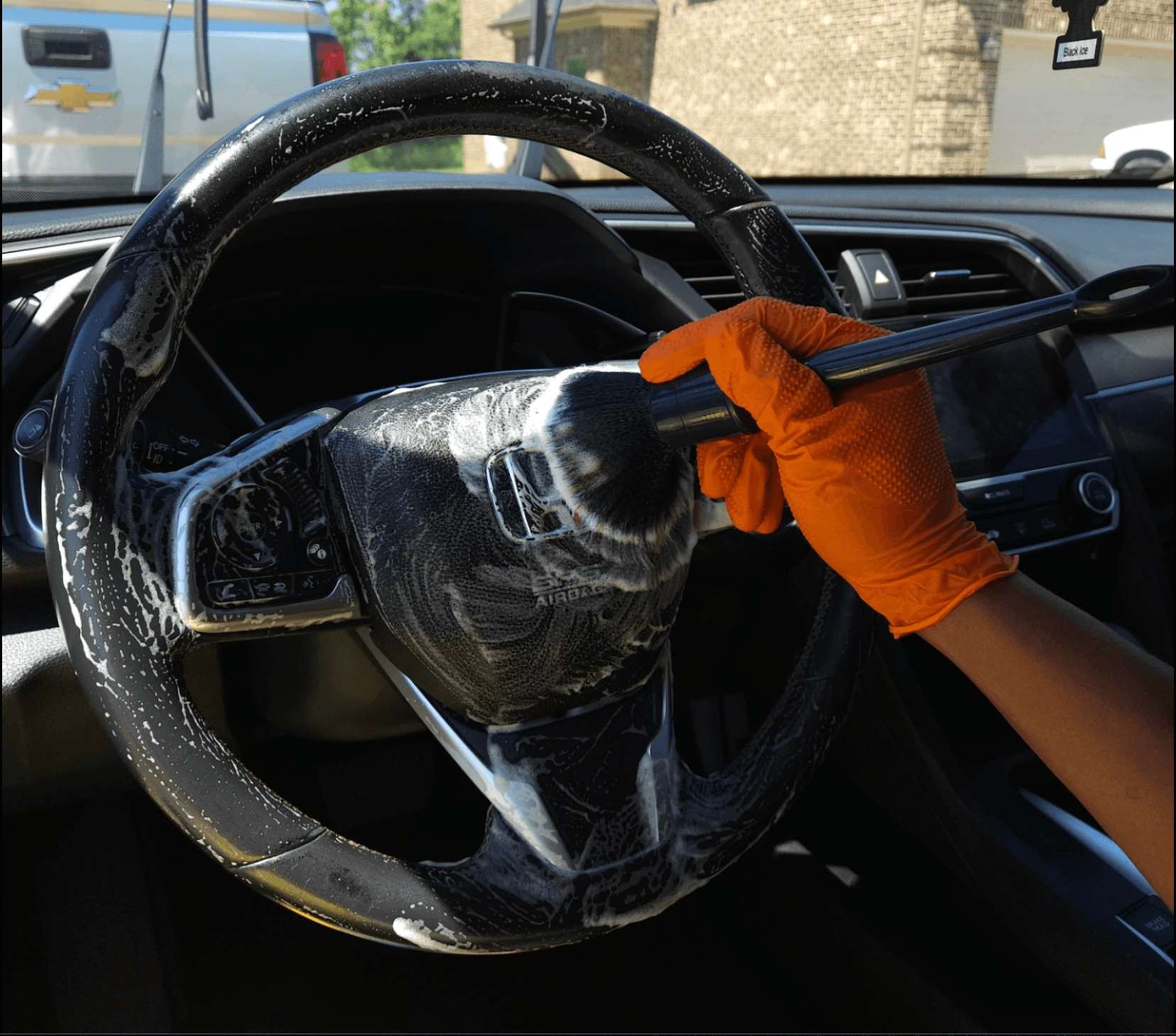 Detailer in nitrile gloves cleaning a foamy steering wheel during a mobile interior detail in Olathe, KS